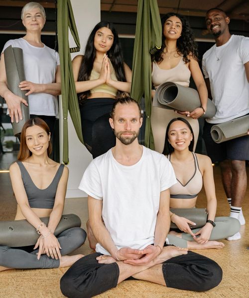 Diverse group of people smiling in a bright yoga class setting.